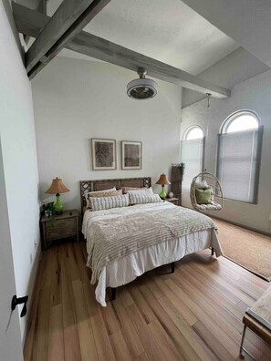 Una camera da letto con un letto grande, due comodini con lampade, una sedia a dondolo e un'ampia finestra ad arco.