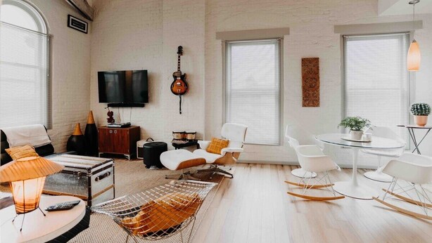 A spacious living room with a high ceiling, a guitar, a television, and a round glass table with chairs. - Skyline View Penthouse Apartment (Mansfield)