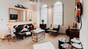 A cozy living room with a leather sofa, a vintage suitcase, and a drum set. - Skyline View Penthouse Apartment (Mansfield)