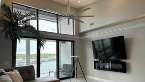A modern living room with a large TV, a ceiling fan, and a balcony with a view of the water. - Topsider Penthouse 511 with Resort Pools (Osage Beach)