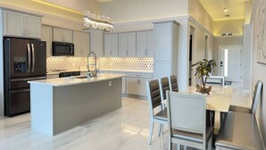 A modern kitchen with a central island, stainless steel appliances, and a dining area with a table and chairs. - Topsider Penthouse 511 with Resort Pools (Osage Beach)