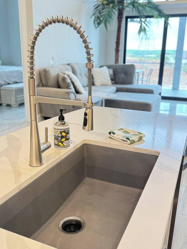 A modern kitchen with a stainless steel sink, a unique faucet, and a decorative mug.