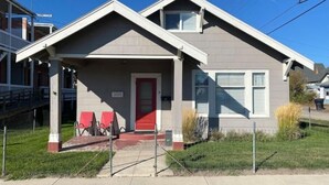 Ein eingeschossiges Haus mit roter Tür, einer überdachten Veranda mit Stühlen und einem kleinen Vorgarten.