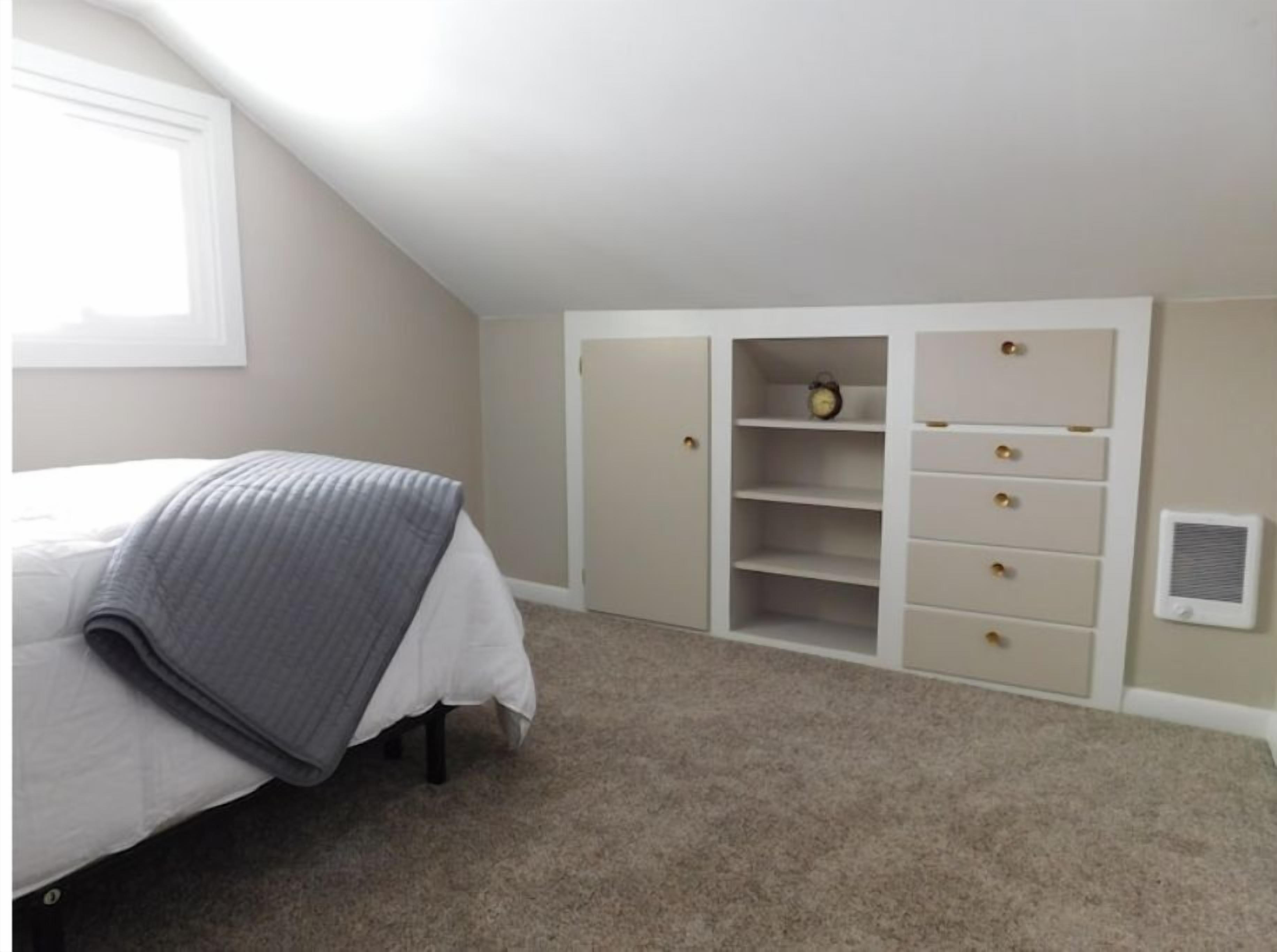 A bedroom with a bed, a dresser, a shelf unit, and a radiator.