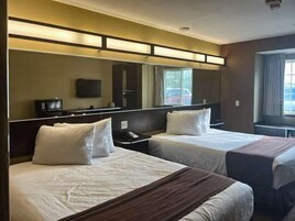 Quarto de hotel com duas camas, um espelho grande, televisão de tela plana e janela com cortinas.