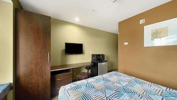 A hotel room with a bed, a desk, a chair, a television, and a microwave.
