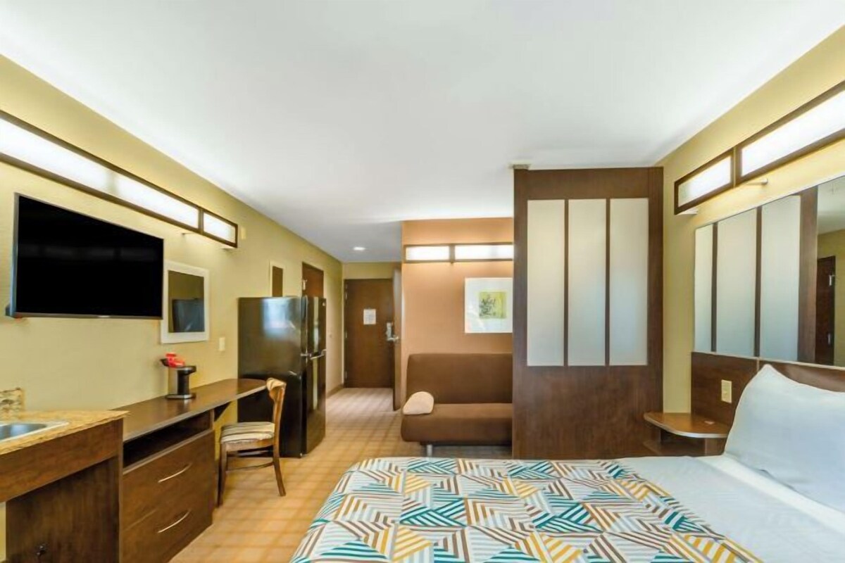 A hotel room with a bed, a desk, a chair, a television, and a refrigerator.