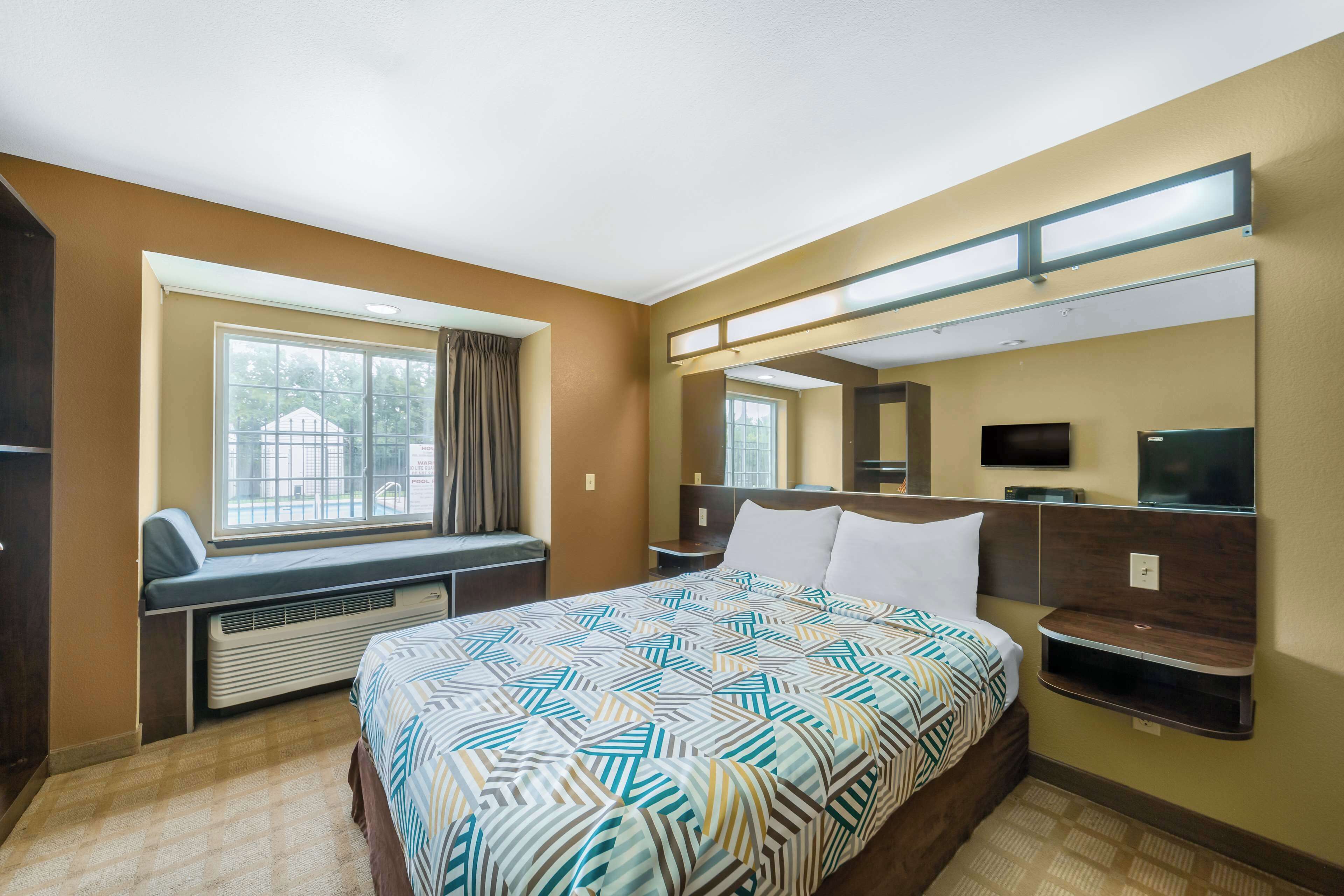 A hotel room with a large bed, a window with a view, a built-in TV, and a desk with a chair.