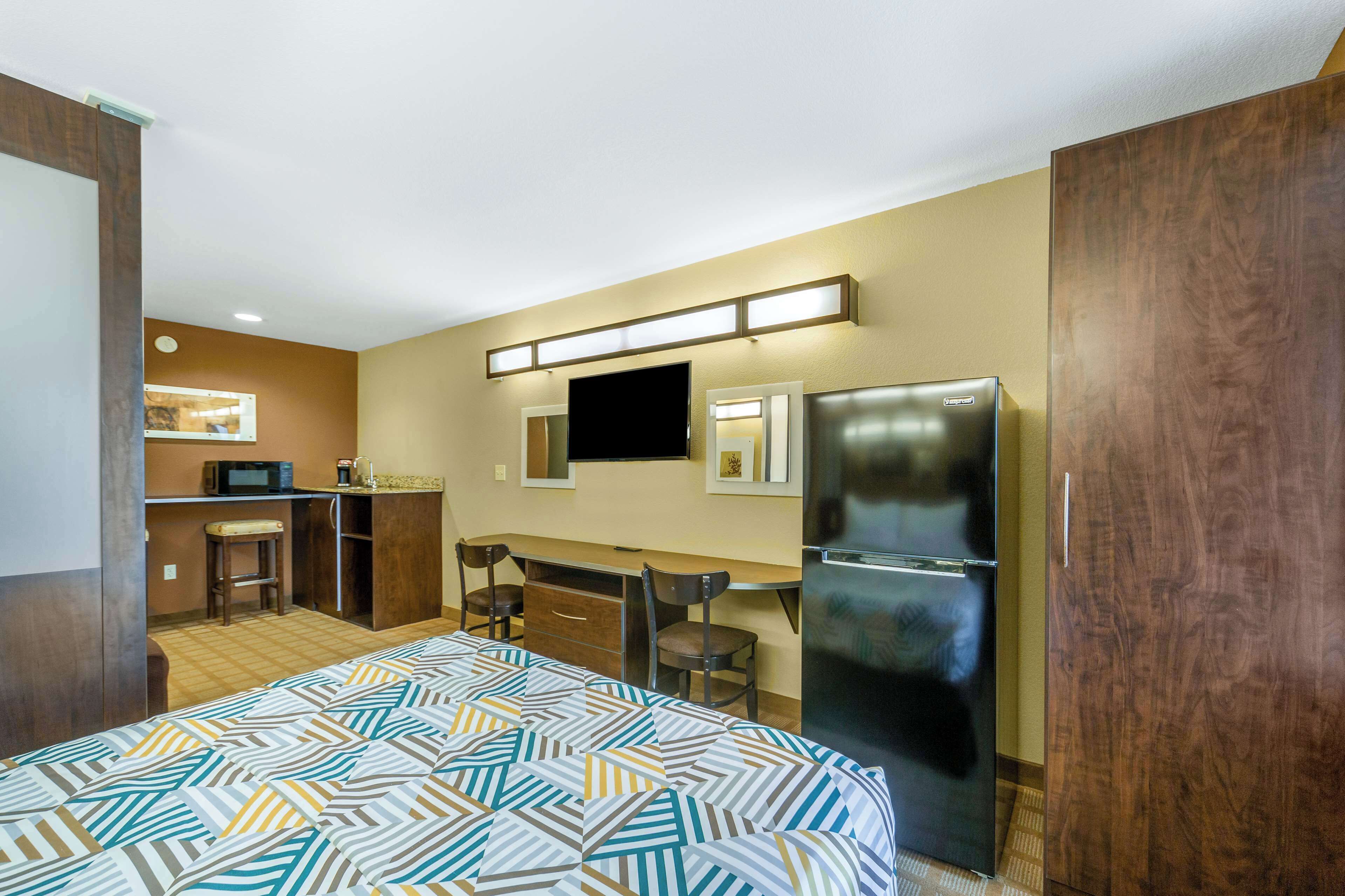 A hotel room with a bed, a desk, a refrigerator, and a kitchenette.