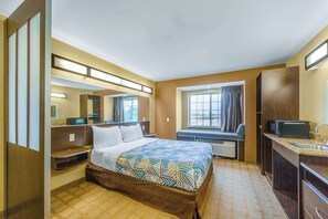 A hotel room with a bed, a desk with a sink, a mirror, and a window with curtains. - Studio 6 Suites - Breaux Bridge, La (Breaux Bridge)
