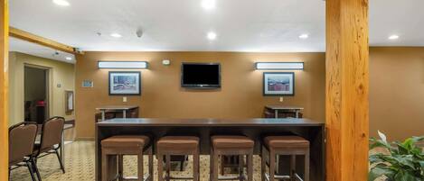 A conference room with a long table, four bar stools, a television, and framed pictures on the wall.