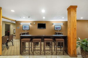 Uma sala de conferências com uma mesa comprida, quatro banquetas, uma televisão e quadros nas paredes.