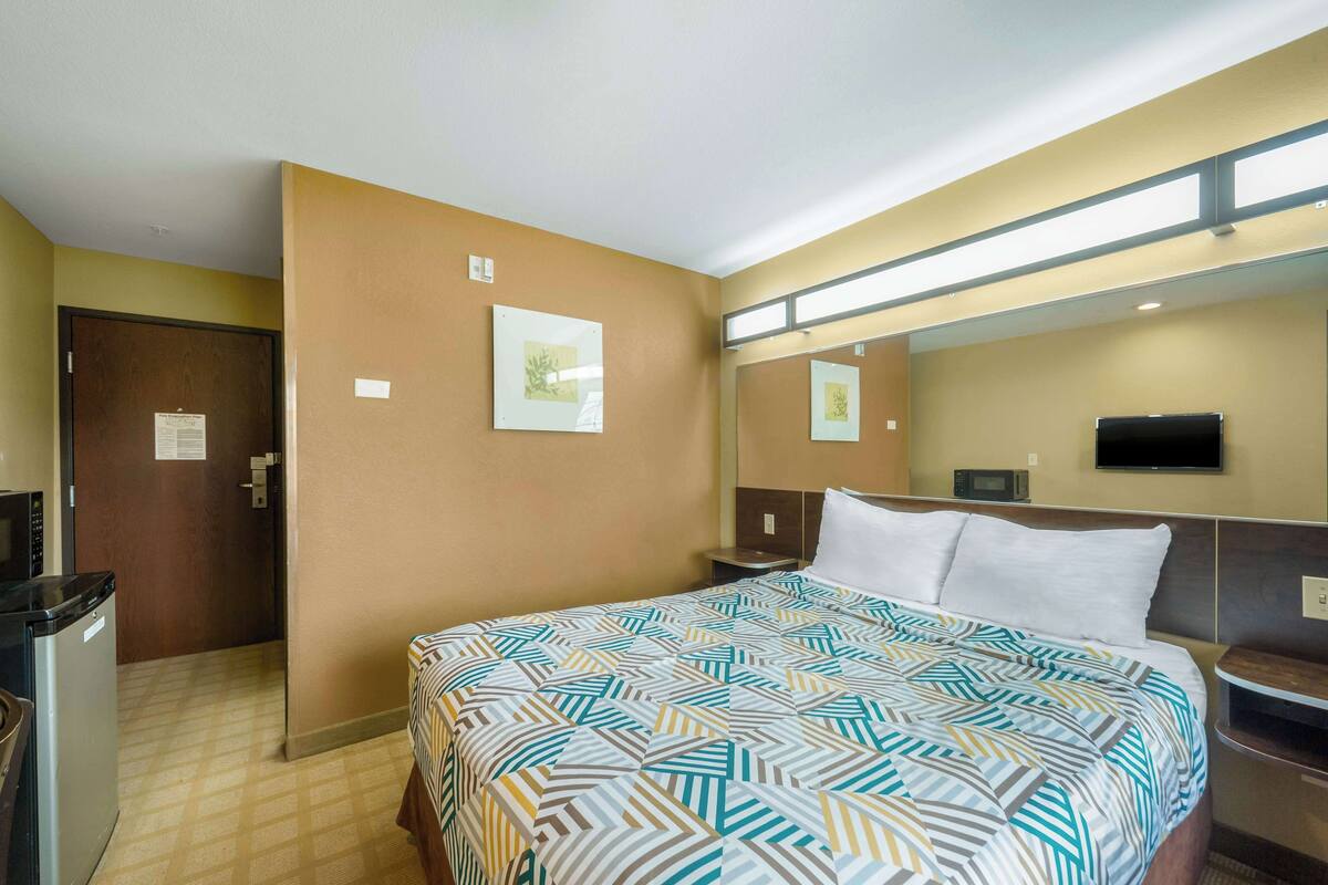 A hotel room with a bed, a desk, a microwave, a TV, and a door.