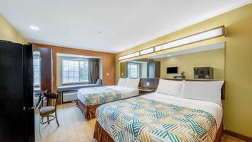 A hotel room with two beds, a desk, a chair, a TV, and a window.