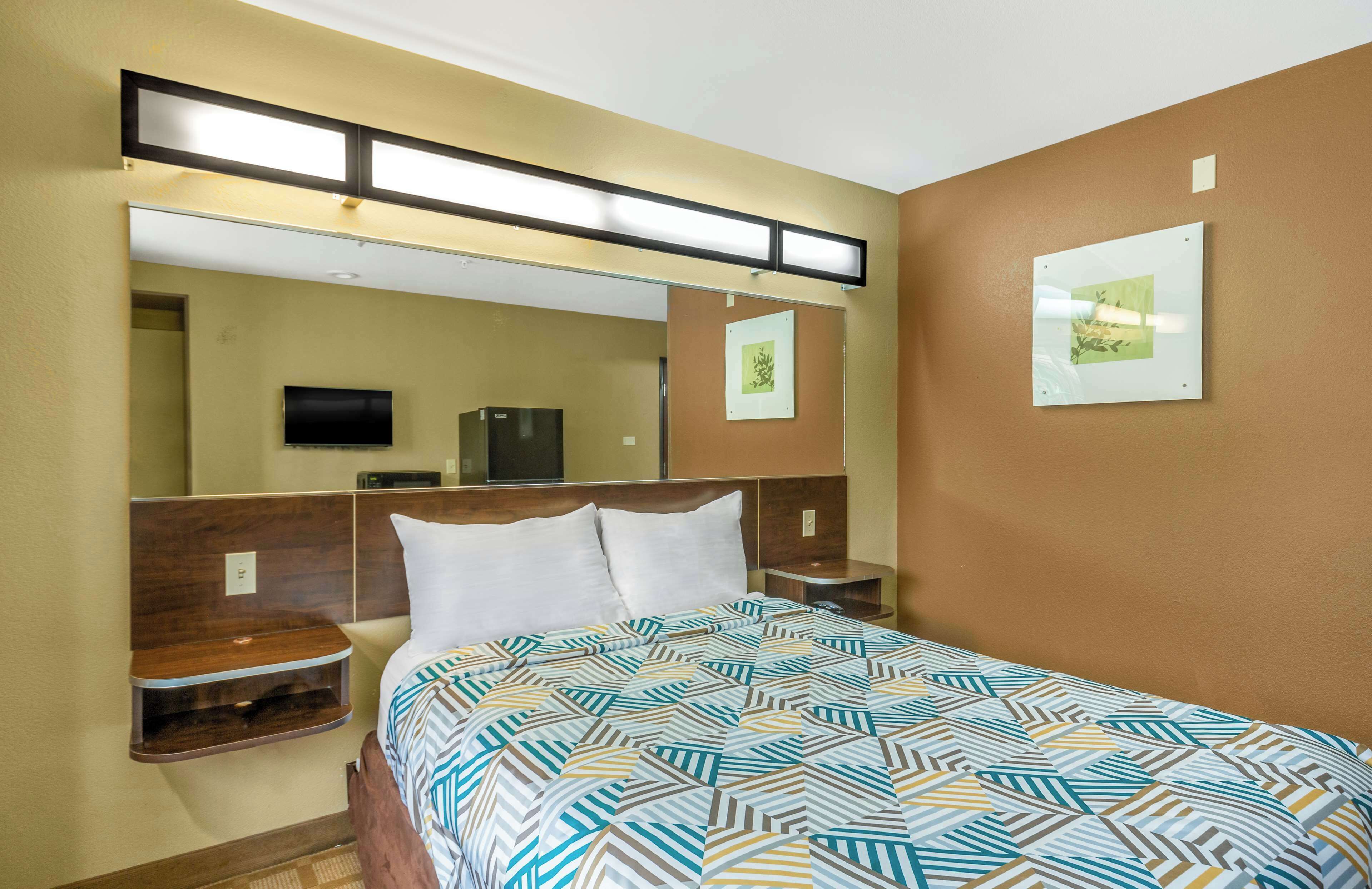 A hotel room with a bed, a TV, a mirror, and a wall-mounted picture.