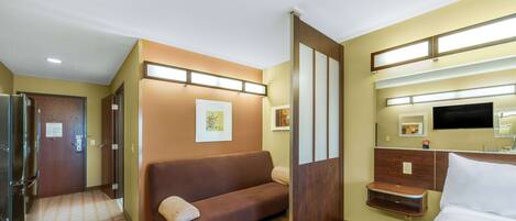 A hotel room with a sofa, a bed, a TV, and a mirror.