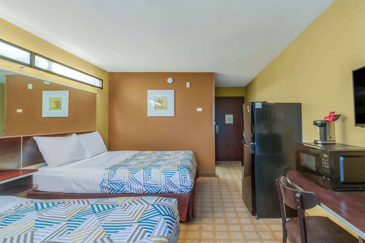 A hotel room with two beds, a desk, a refrigerator, and a microwave.