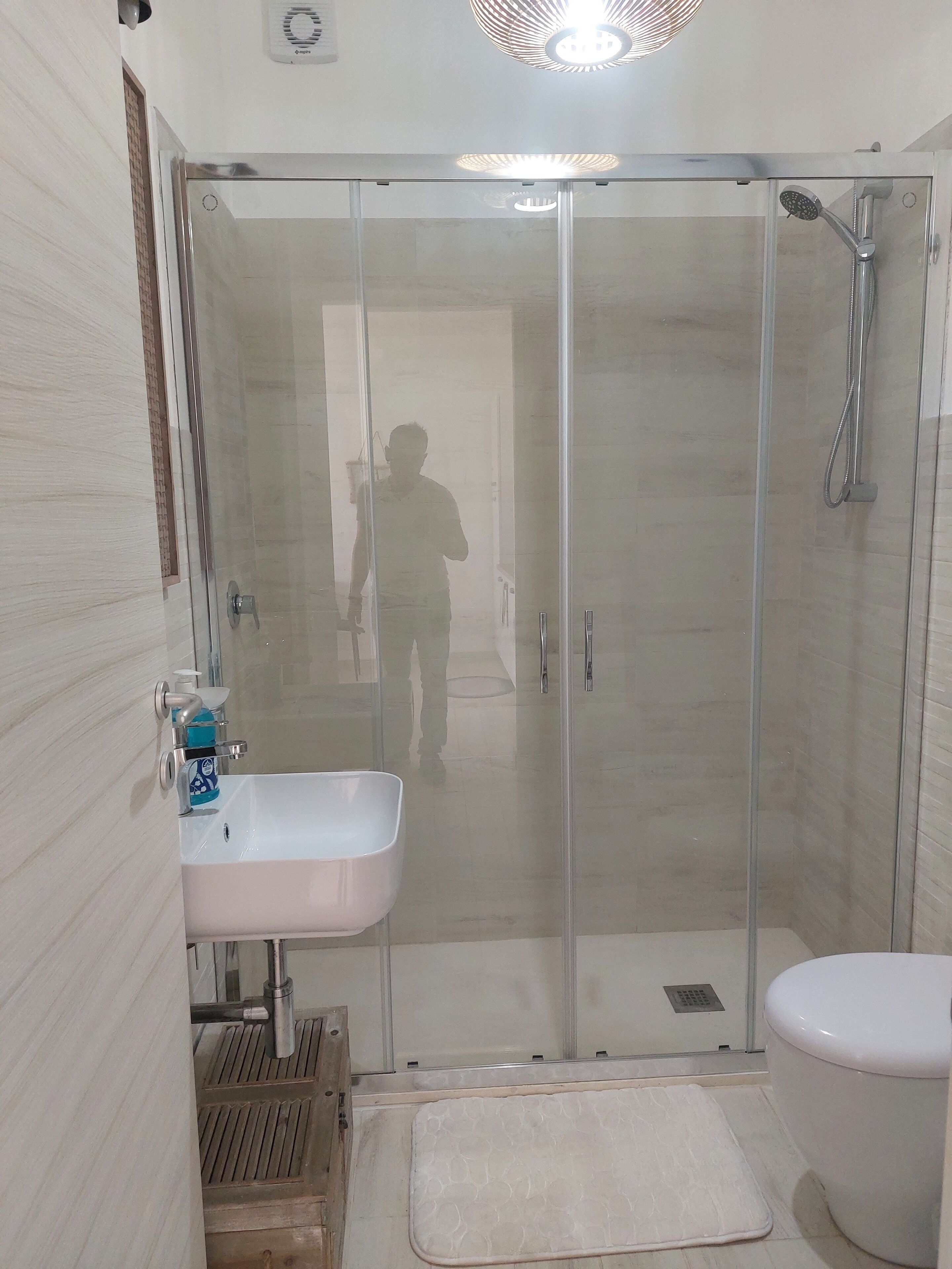 A bathroom with a glass-enclosed shower, a sink with a soap dispenser, and a toilet.
