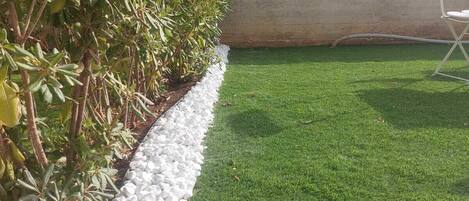 A landscaped garden with a hedge, white pebbles, and green grass.