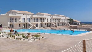 Un resort con una grande piscina, edifici a più piani e vista libera sul mare.
