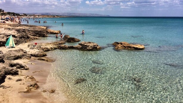 Una spiaggia con acque cristalline, costa rocciosa e persone che nuotano.