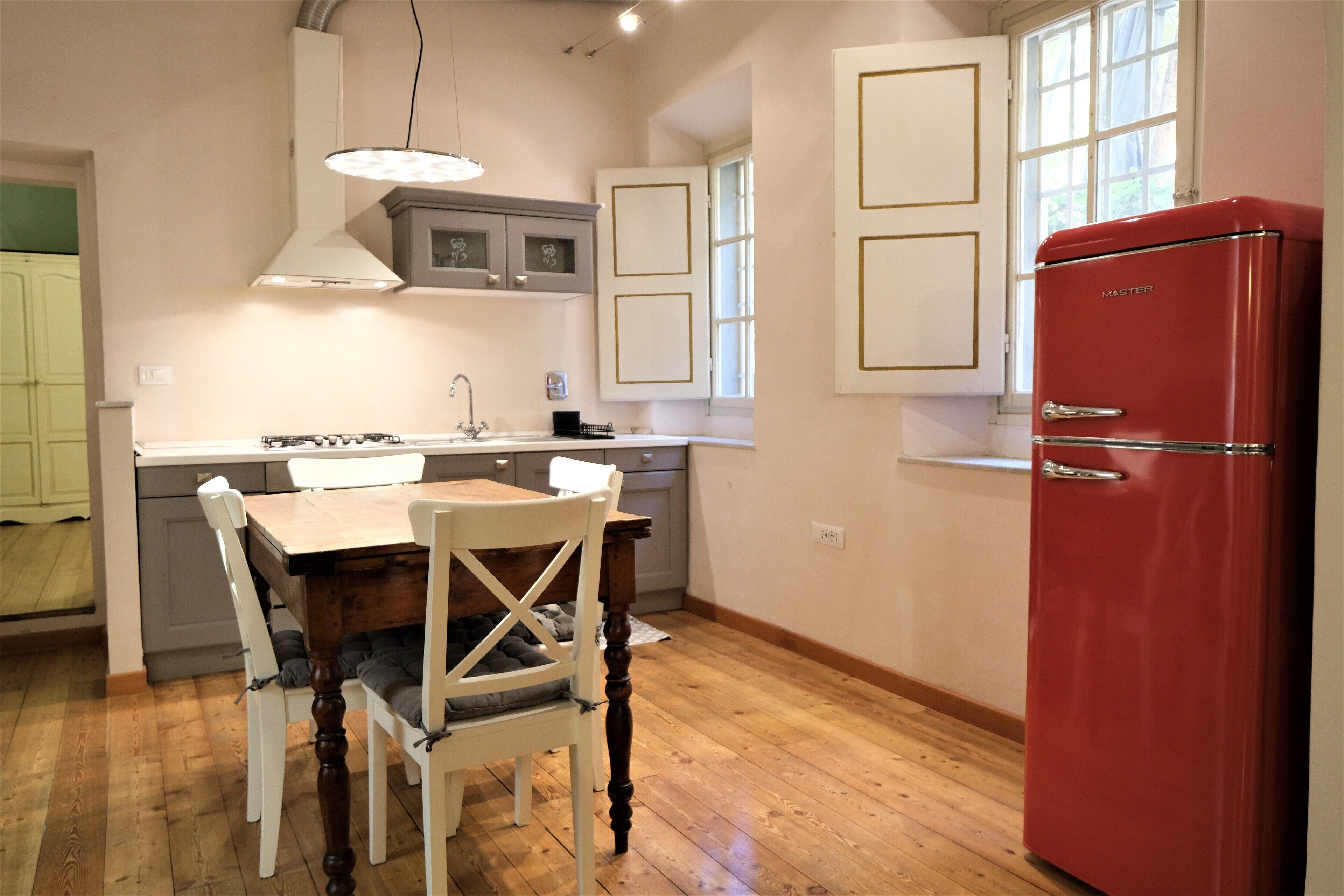 Une cuisine avec une table à manger en bois, des chaises, un réfrigérateur rouge et une fenêtre donnant sur un beau paysage.