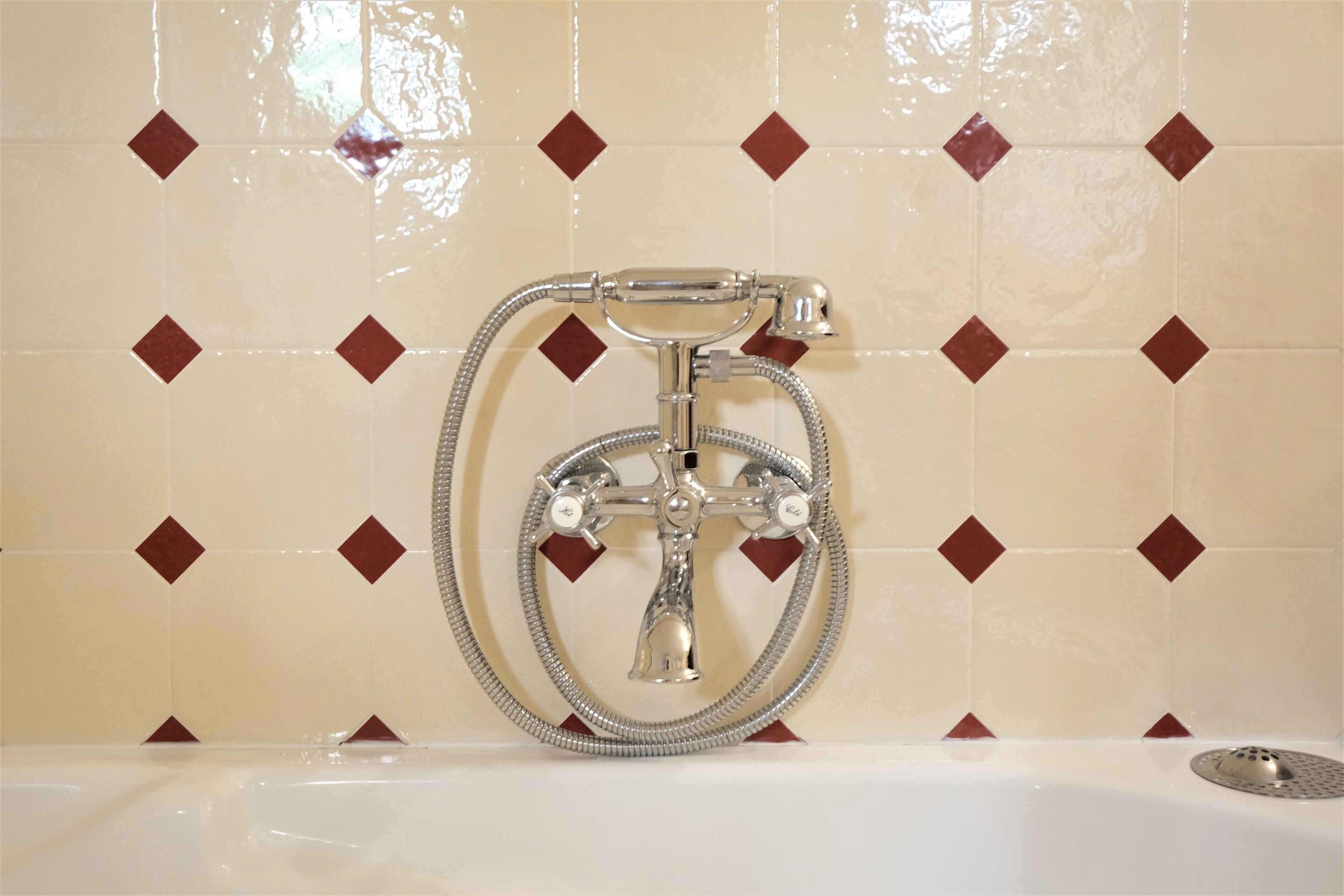 A bathroom with a shower and a bathtub, featuring a tiled wall with a diamond pattern.