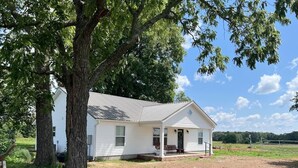 A white single-story house with a porch, surrounded by trees and open fields. - The Red Gate - Branson & Eureka!
 (Green Forest)