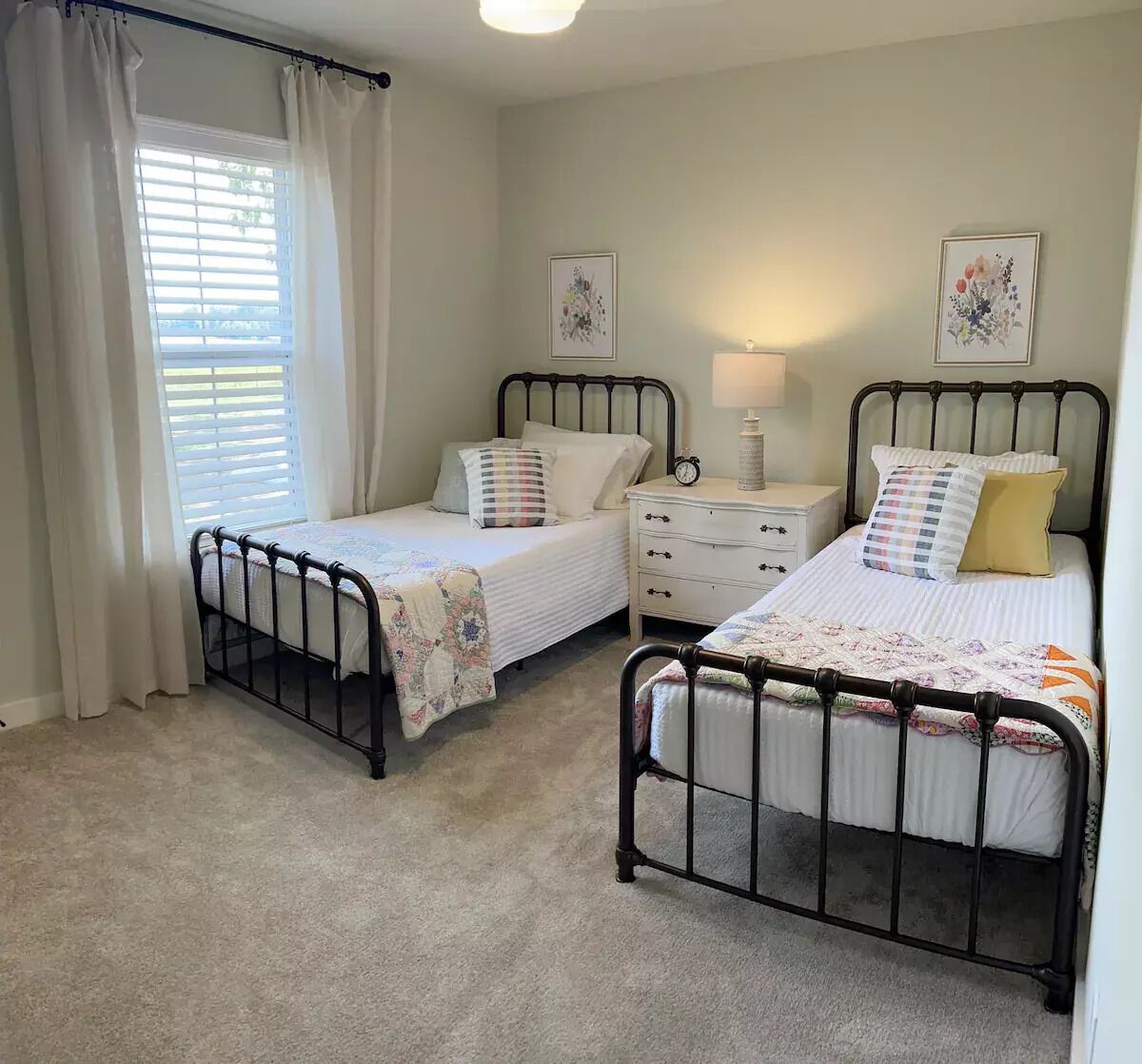 A bedroom with two single beds, a nightstand, a dresser, and a window with curtains.