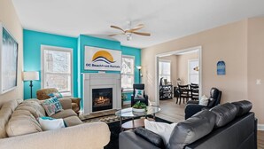 A living room with a fireplace, a ceiling fan, and a sign for OC Beachfront Rentals. - ⭐️ Brand New, Fully Renovated Home Steps to Boardwalk Beach (Ocean City)