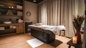 Relax in a serene space with a massage table, wooden shelf, and calming candle.