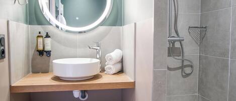 A modern bathroom with a round mirror, sink, and shower.