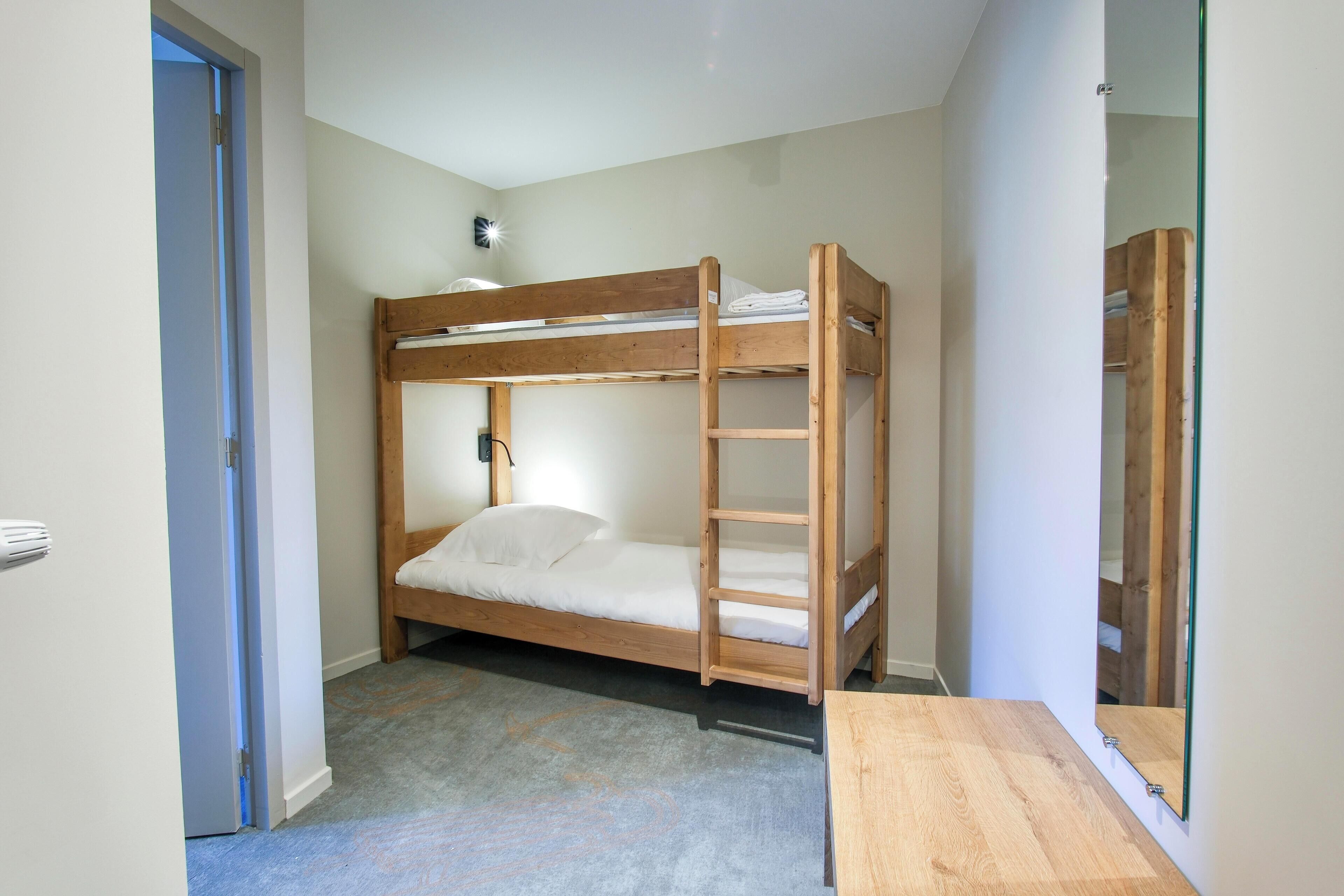 Ein Schlafraum mit Etagenbett, einem kleinen Nachttisch und einem Spiegel an der Wand.