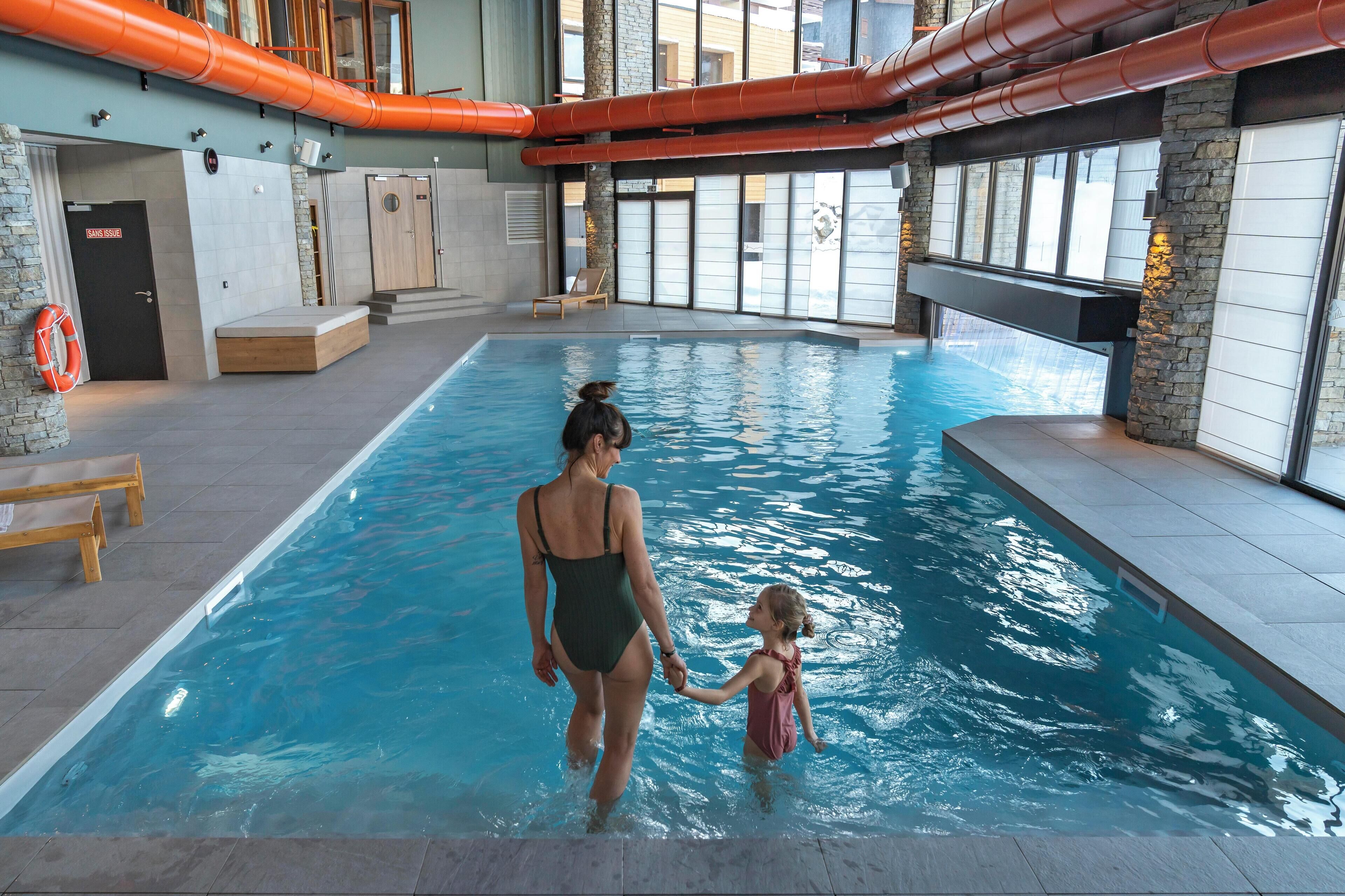 Una piscina interior amb una dona i un nen agafats de la mà.
