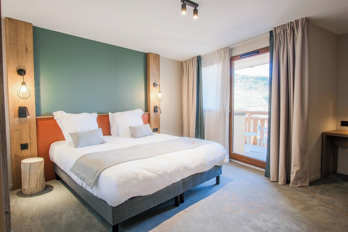 A hotel room with a large bed, a wooden headboard, a nightstand, and a view of the outdoors through a sliding door.