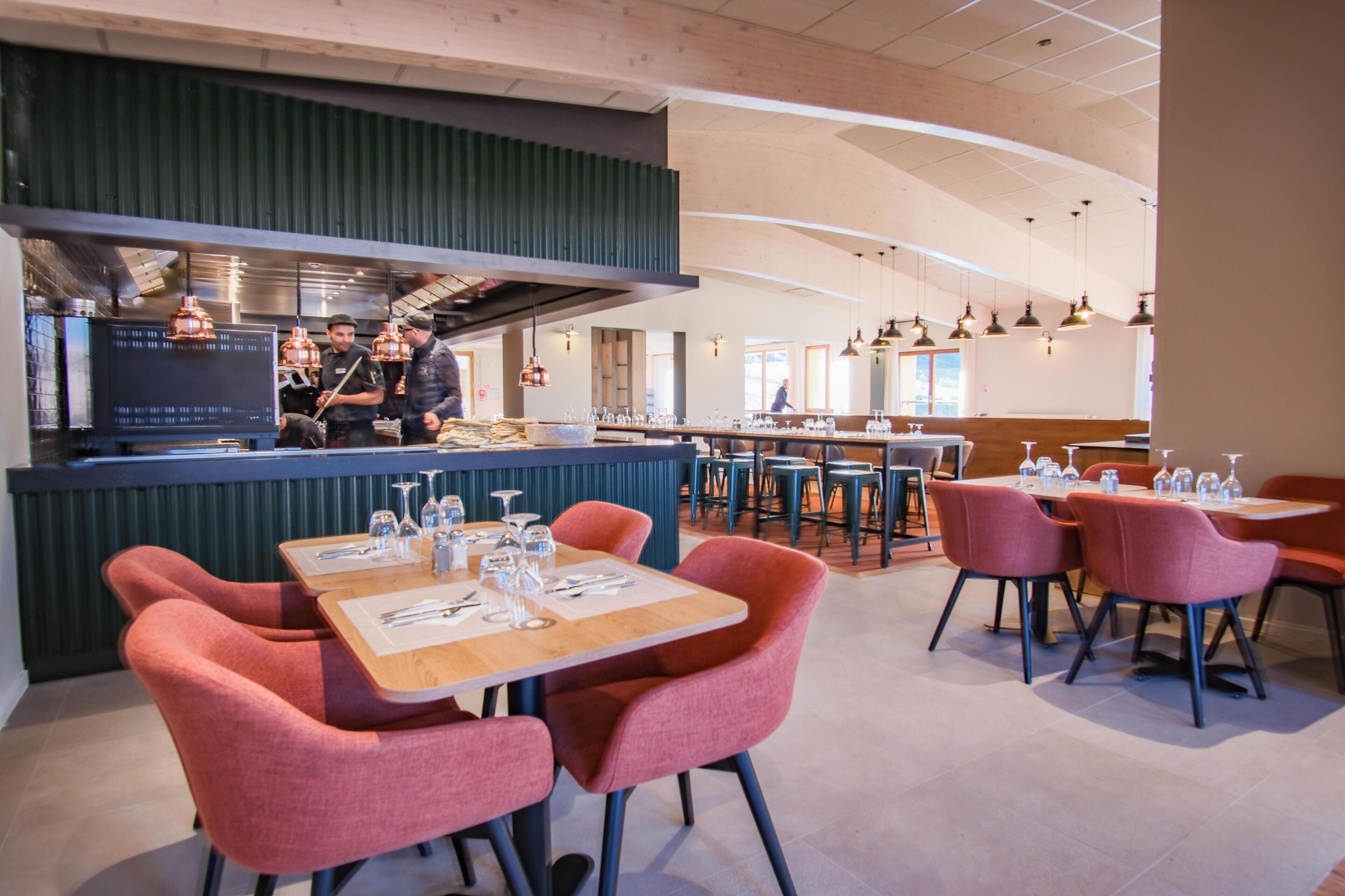 A restaurant interior with a bar area, seating with tables and chairs, and a modern kitchen in the background.