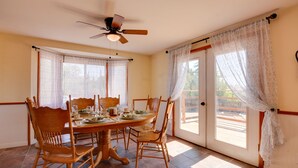 A dining area with a wooden table and chairs, a ceiling fan, and large windows with curtains.