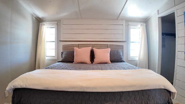 Una camera da letto con un letto, due finestre, una testiera in legno e un soffitto bianco.