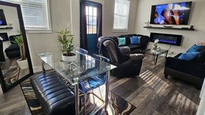 Ein modernes Wohnzimmer mit einem Glastisch, einem schwarzen Ledersofa und einem an der Wand befestigten Flachbildfernseher.