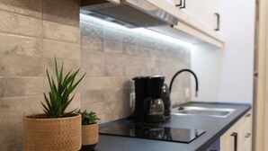 A modern kitchen with a black countertop, a coffee maker, and two potted plants. - Flare Studio  (Corfu)