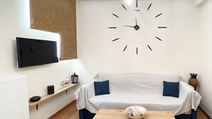 A modern living room with a sofa, a flat-screen TV, a wall clock, a small table, and a decorative lantern. - Flare Studio  (Corfu)