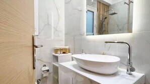 A modern bathroom with a white vanity, a large mirror, and a wooden floor. - Flare Studio  (Corfu)