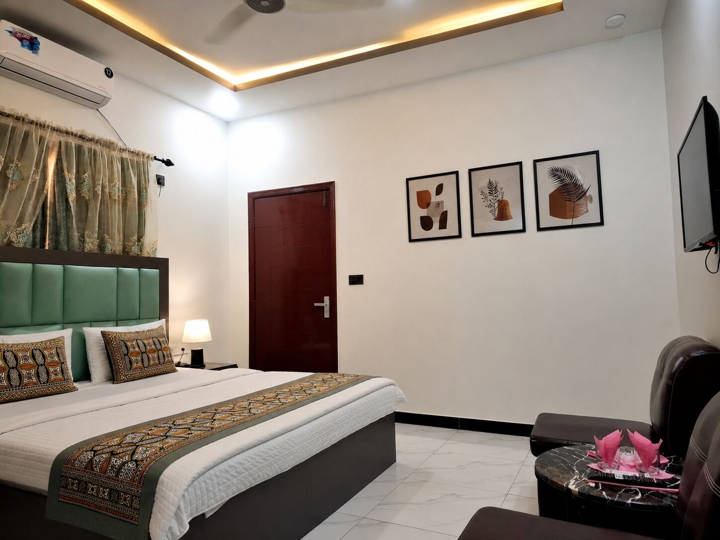 A hotel room with a bed, a desk, a chair, a TV, and artwork on the wall.