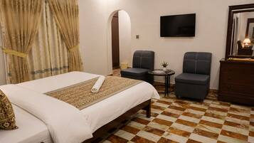 Habitación de hotel con cama, dos sillones, una mesita, televisión y un reloj en la pared.