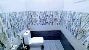 Un baño con inodoro blanco, zona de ducha y pared con diseño de mármol.