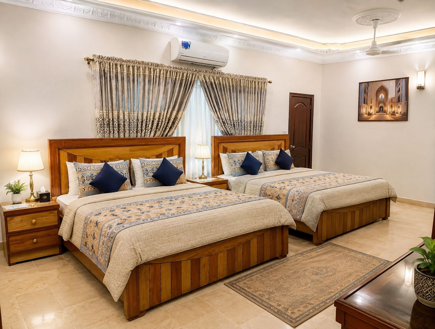 Habitación de hotel con dos camas de madera, una mesita de noche con lámpara, aire acondicionado en la pared y un amplio ventanal con cortinas.