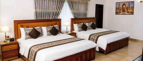 Una habitación de hotel con dos camas, una mesita de noche con lámpara, aire acondicionado de pared y un cuadro enmarcado.