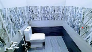 A bathroom with a white toilet, a shower area, and a marble-patterned wall.