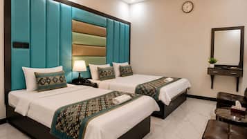 A hotel room with two beds, a bedside table with a lamp, a clock on the wall, a mirror, and a seating area with a table.
