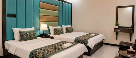A hotel room with two beds, a bedside table with a lamp, a clock on the wall, a mirror, and a seating area with a table.